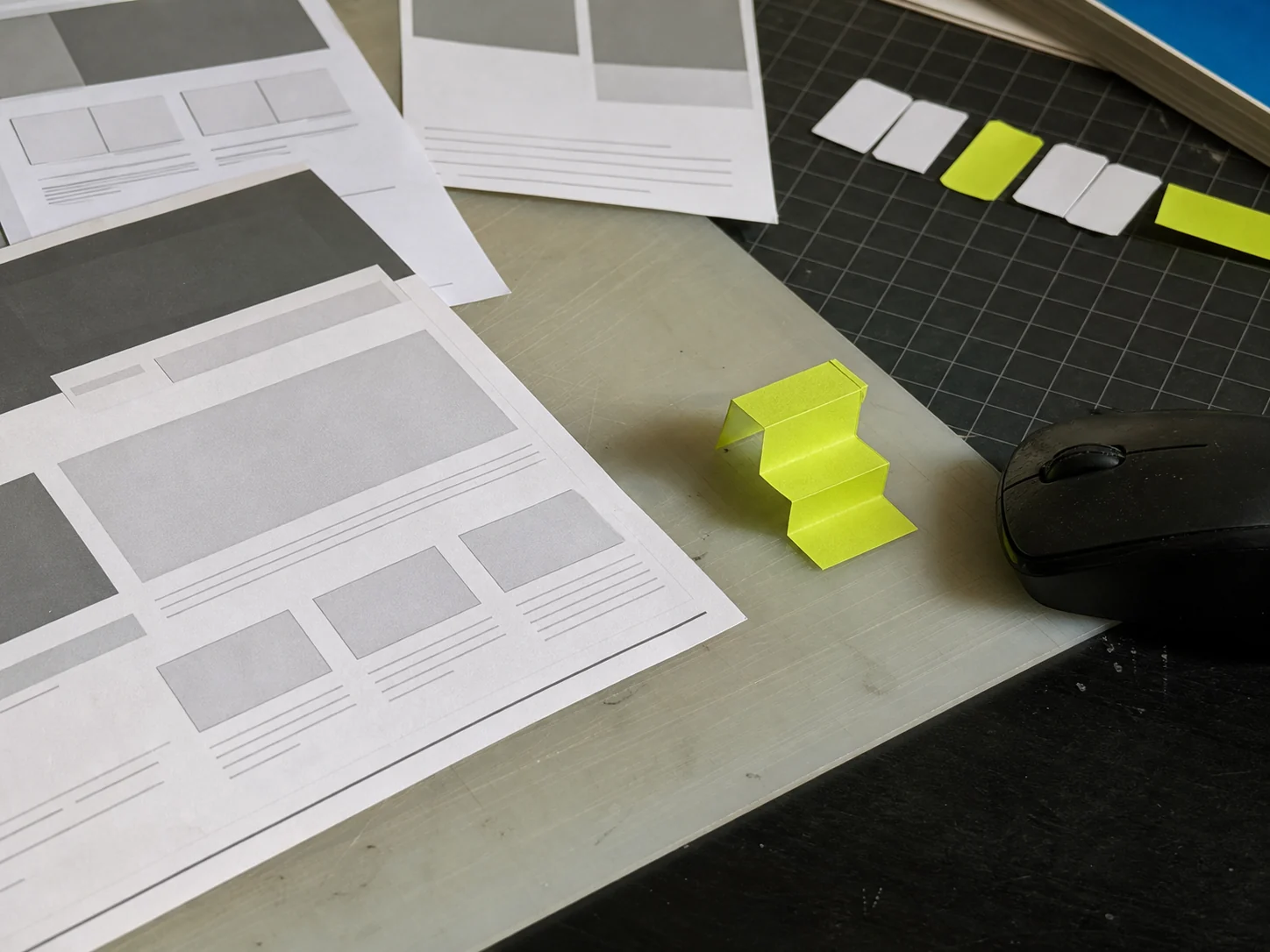 Mesa de criação com wireframes impressos e uma pequena escada de papel verde.
